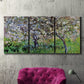 Three-panel canvas wall art featuring apple trees blooming beside water, displayed in a living room above a suede accent chair.