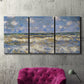 Three-panel canvas wall art featuring rough sea with crashing waves, displayed in a living room above a suede accent chair.