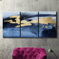 Three-panel canvas wall art featuring coastal shoreline with warm light, displayed in a living room above a suede accent chair.