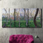 Three-panel canvas wall art featuring spring landscape along river, displayed in a living room above a suede accent chair.