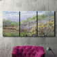 Three-panel canvas wall art featuring spring orchard in full bloom, displayed in a living room above a suede accent chair.