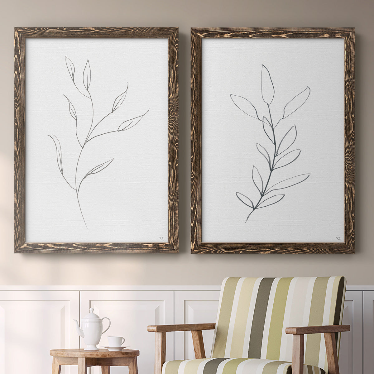 Set of two walnut barnwood framed canvas prints depicting two minimalist botanical line drawings featuring single continuous-line leafy branches above a sideboard in a cozy sitting room.