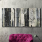 Three-panel canvas wall art featuring vertical abstract tree forms, displayed in a living room above a suede accent chair.