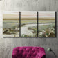Three-panel canvas wall art featuring pastoral fields under soft sunrise, displayed in a living room above a suede accent chair.
