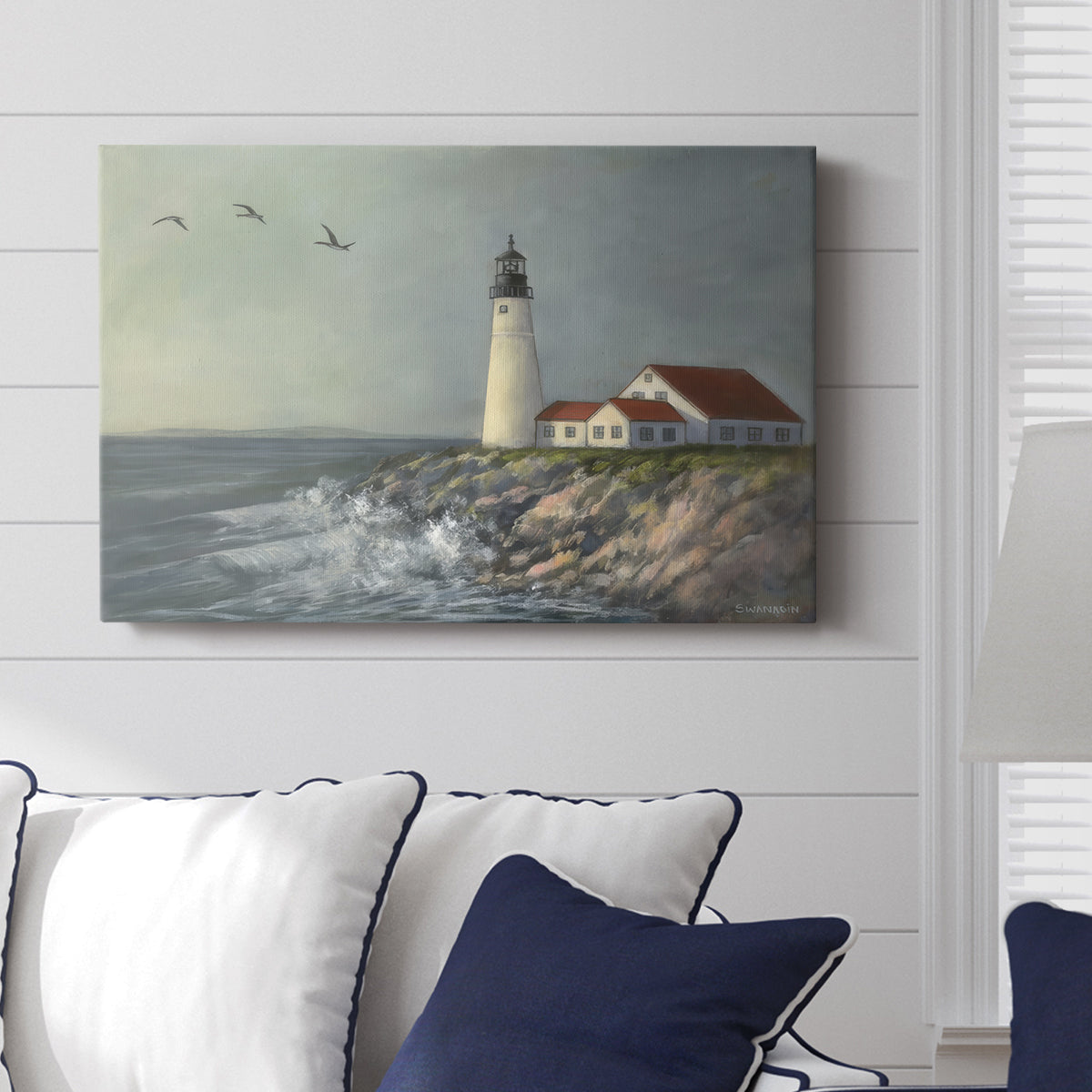 Lighthouse stands tall against crashing waves at a coastal location with birds flying overhead during a calm day