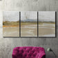 Three-panel canvas wall art featuring golden hour light over landscape, displayed in a living room above a suede accent chair.