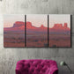Three-panel canvas wall art featuring red rock desert formations at dusk, displayed in a living room above a suede accent chair.