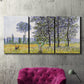 Three-panel canvas wall art featuring sunlight filtering through tall poplars, displayed in a living room above a suede accent chair.