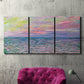 Three-panel canvas wall art featuring sunset reflections across calm sea, displayed in a living room above a suede accent chair.