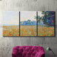 Three-panel canvas wall art featuring oat field with scattered poppies, displayed in a living room above a suede accent chair.