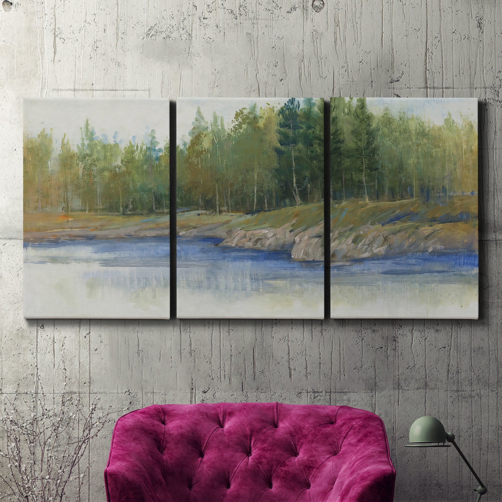Three-panel canvas wall art featuring riverbank landscape with trees, displayed in a living room above a suede accent chair.