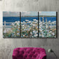 Three-panel canvas wall art featuring coastal garden overlooking bay, displayed in a living room above a suede accent chair.
