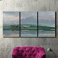 Three-panel canvas wall art featuring twilight landscape with fading light, displayed in a living room above a suede accent chair.