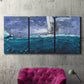 Three-panel canvas wall art featuring sailboats moving across water, displayed in a living room above a suede accent chair.