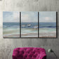 Three-panel canvas wall art featuring shore birds searching along beach, displayed in a living room above a suede accent chair.