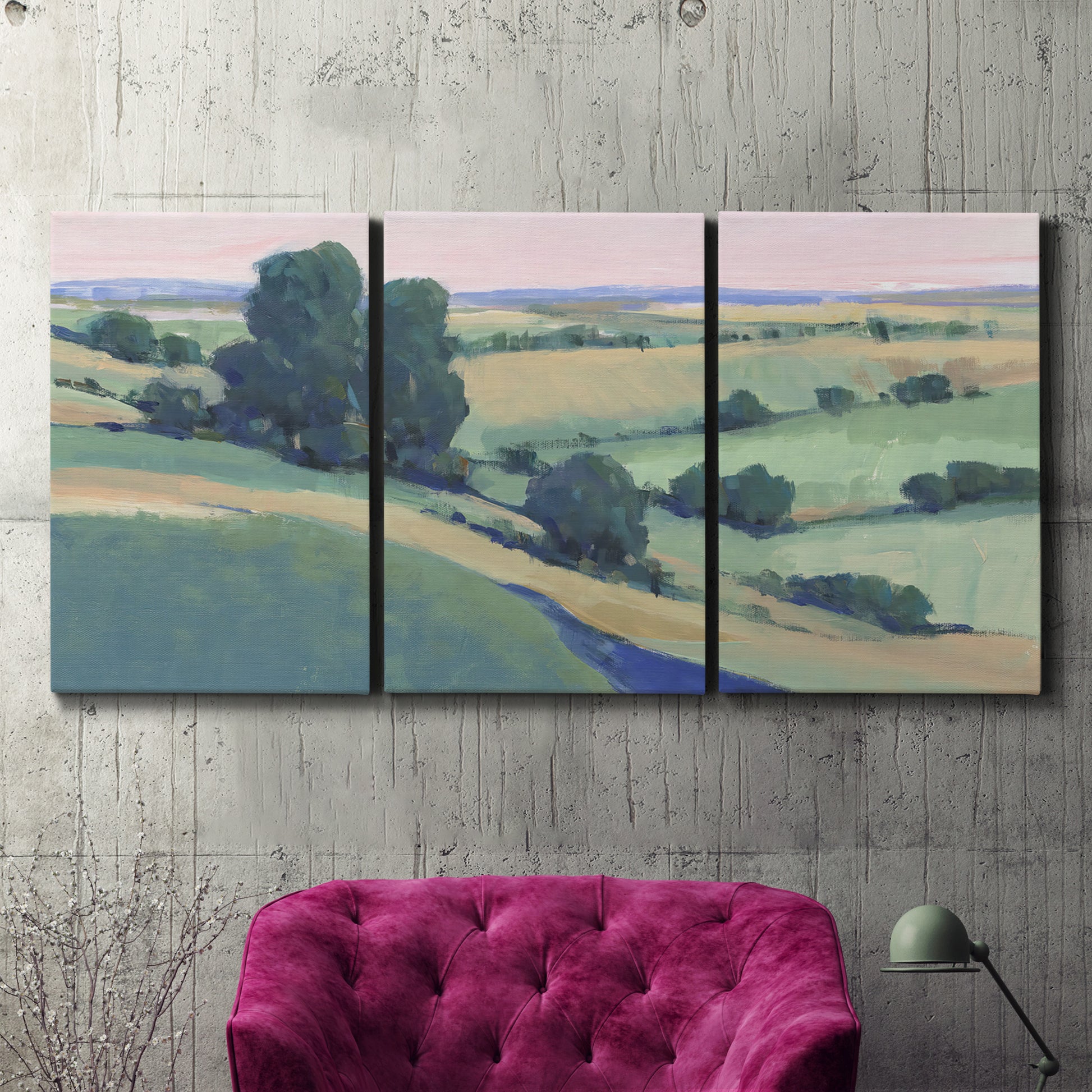 Three-panel canvas wall art featuring pastoral countryside with rocky outcrop, displayed in a living room above a suede accent chair.