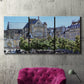 Three-panel canvas wall art featuring gothic church within city setting, displayed in a living room above a suede accent chair.