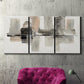 Three-panel canvas wall art featuring urban abstract watercolor oasis, displayed in a living room above a suede accent chair.