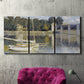Three-panel canvas wall art featuring bridge crossing broad river, displayed in a living room above a suede accent chair.