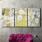 Three-panel canvas wall art featuring vintage inspired floral abstraction, displayed in a living room above a suede accent chair.