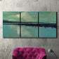 Three-panel canvas wall art featuring calm harbor water with glowing horizon, displayed in a living room above a suede accent chair.