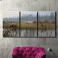 Three-panel canvas wall art featuring wildlife walking through open field, displayed in a living room above a suede accent chair.