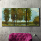 Three-panel canvas wall art featuring tall trees lining open landscape, displayed in a living room above a suede accent chair.