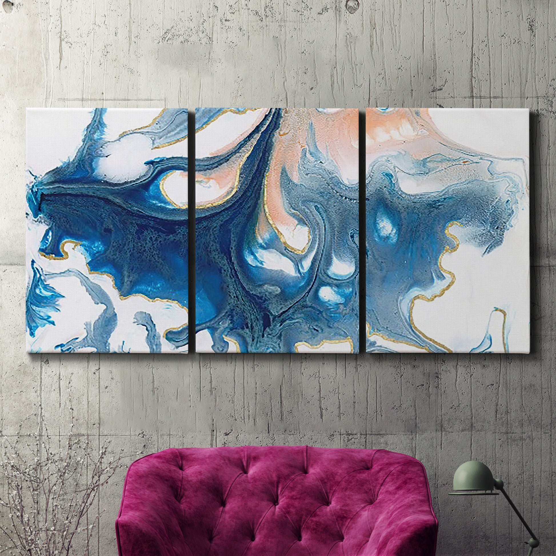 Three-panel canvas wall art featuring flowing blue abstract movement, displayed in a living room above a suede accent chair.
