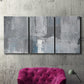 Three-panel canvas wall art featuring cool toned industrial abstract blues, displayed in a living room above a suede accent chair.