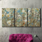 Three-panel canvas wall art featuring abstract flowering vine pattern, displayed in a living room above a suede accent chair.
