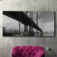 Three-panel canvas wall art featuring manhattan bridge industrial cityscape, displayed in a living room above a suede accent chair.