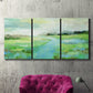Three-panel canvas wall art featuring gentle stream winding through trees, displayed in a living room above a suede accent chair.
