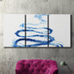 Three-panel canvas wall art featuring indigo abstract vapor watercolor, displayed in a living room above a suede accent chair.