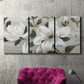 Three-panel canvas wall art featuring soft southern floral charm, displayed in a living room above a suede accent chair.