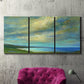 Three-panel canvas wall art featuring coastal shoreline with soft waves, displayed in a living room above a suede accent chair.