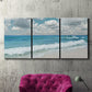 Three-panel canvas wall art featuring tropical beach scene with turquoise water, displayed in a living room above a suede accent chair.