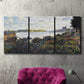Three-panel canvas wall art featuring river with boats and shoreline, displayed in a living room above a suede accent chair.