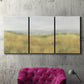 Three-panel canvas wall art featuring pastoral wheat field landscape, displayed in a living room above a suede accent chair.