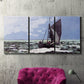 Three-panel canvas wall art featuring stormy sea with crashing waves, displayed in a living room above a suede accent chair.