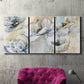 Three-panel canvas wall art featuring delicate watercolor floral blooms, displayed in a living room above a suede accent chair.