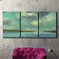 Three-panel canvas wall art featuring still lagoon water beneath open sky, displayed in a living room above a suede accent chair.