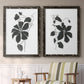 Set of two black barnwood framed canvas prints depicting two minimalist botanical prints featuring black leafy vine silhouettes above a sideboard in a cozy sitting room.