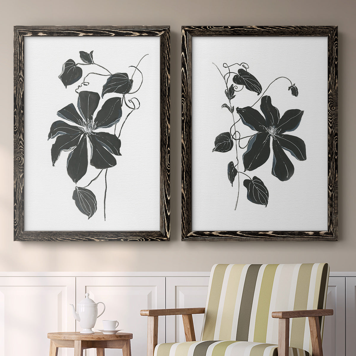 Set of two black barnwood framed canvas prints depicting two minimalist botanical prints featuring black leafy vine silhouettes above a sideboard in a cozy sitting room.