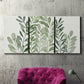 Three-panel canvas wall art featuring foraged leafy greens botanical study, displayed in a living room above a suede accent chair.
