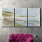 Three-panel canvas wall art featuring coastal cove with calm water, displayed in a living room above a suede accent chair.