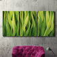 Three-panel canvas wall art featuring close view of tall green grass blades, displayed in a living room above a suede accent chair.