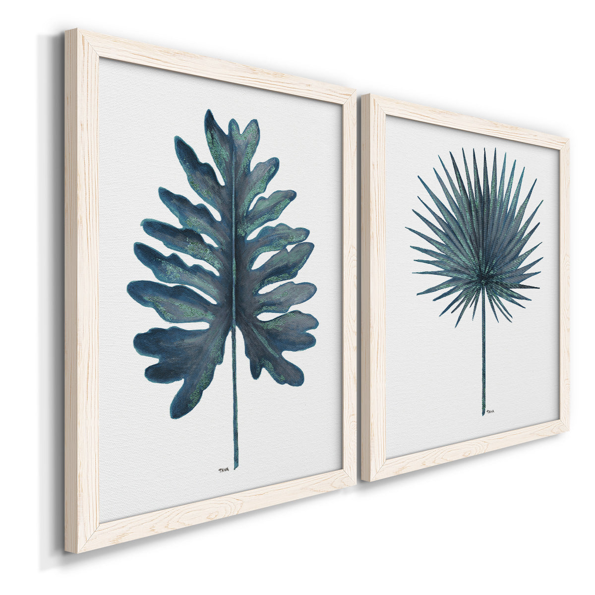 Angled view of a set of two white barnwood framed canvas prints featuring two modern botanical illustrations featuring large blue-green tropical leaves.