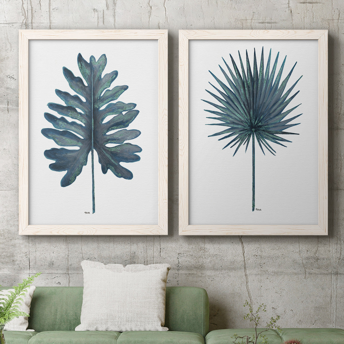 Set of two white barnwood framed canvas prints depicting a coordinated art pair of large blue-green tropical leaves rendered as modern botanical illustrations above a sofa in a modern living room.