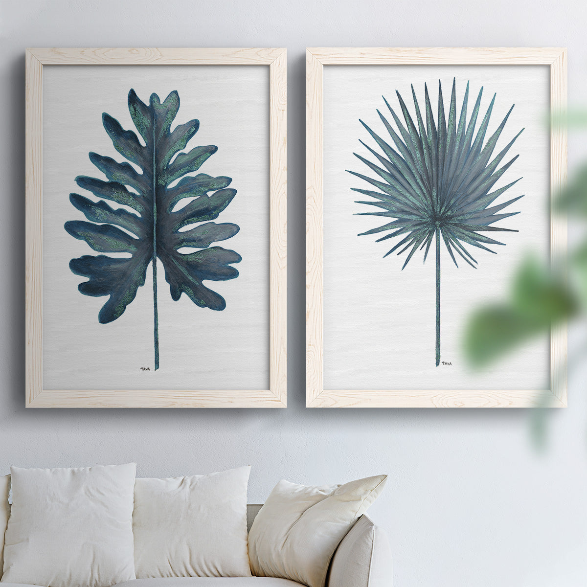 Set of two white barnwood framed canvas prints depicting fan palms, broad philodendron leaves, and crisp white grounds arranged across two complementary compositions above a sofa in a bright living space.
