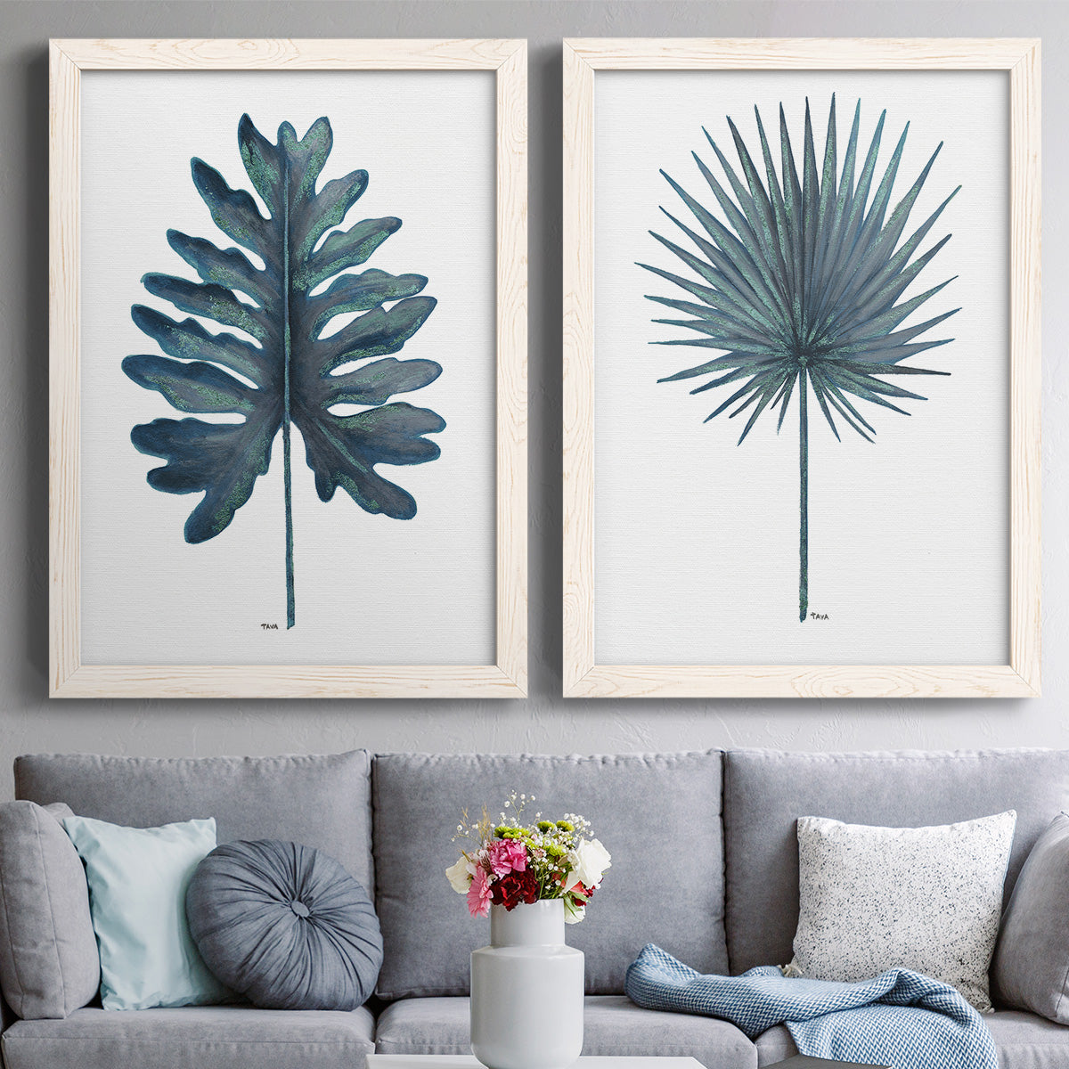 Set of two white barnwood framed canvas prints depicting paired modern botanical illustrations with fan palms, broad philodendron leaves, and crisp white grounds above a sofa in a contemporary living room.